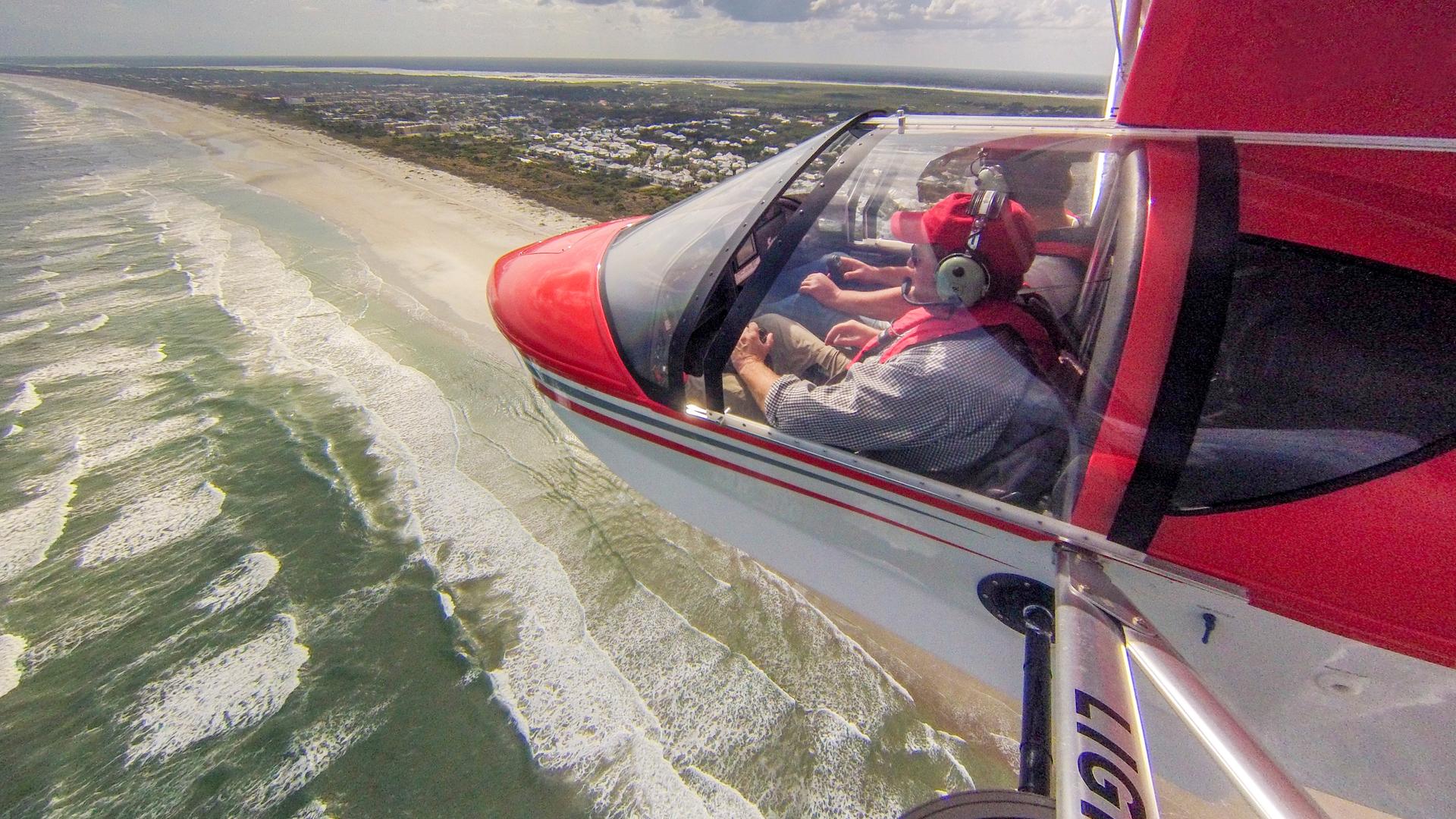 Red plane flying over white sand beach